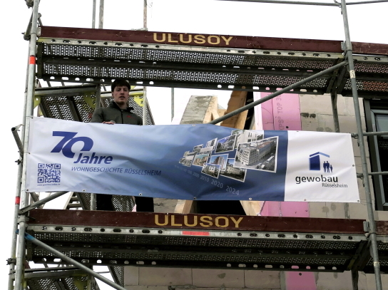 Der Polier Jonas Vetter auf dem Gerüst mit dem Banner der gewobau bei seinem Richtspruch